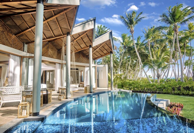 This pool at Waldorf Astoria Seychelles Platte Island is flanked by white chairs and palm trees.